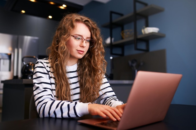 Giovane donna libera professionista che lavora con il laptop da casa seduta in soggiorno Femmina che digita sulla tastiera per un progetto di lavoro remoto Ragazza focalizzata che utilizza il computer per studiare online facendo i compiti