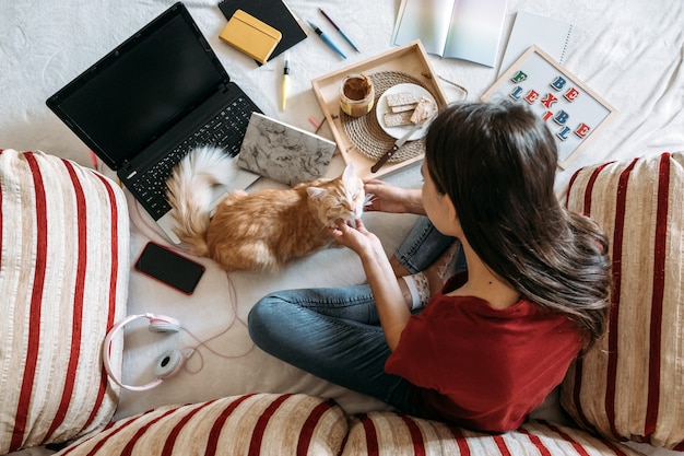 Giovane donna libera professionista che lavora in ufficio a casa con un computer portatile e un gatto che lavora online a distanza