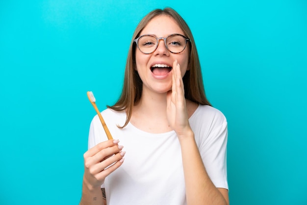 Giovane donna lituana che pulisce i denti su sfondo isolato gridando con la bocca spalancata