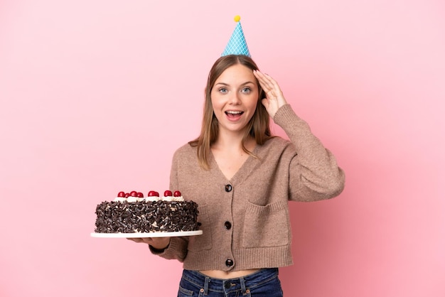 Giovane donna lituana che tiene la torta di compleanno isolata su fondo rosa con l'espressione di sorpresa