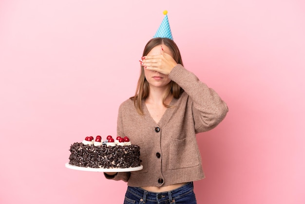 Giovane donna lituana che tiene la torta di compleanno isolata su sfondo rosa che copre gli occhi con le mani Non voglio vedere qualcosa