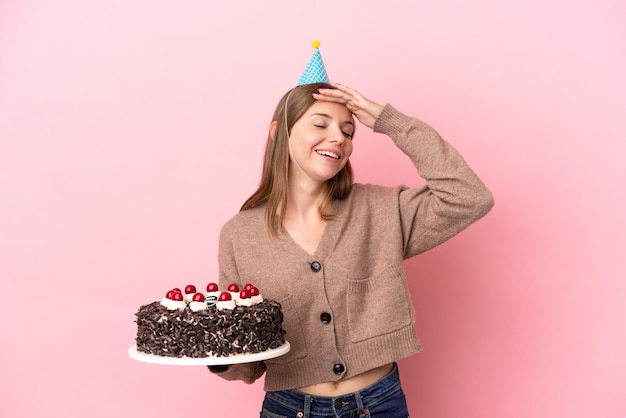 Giovane donna lituana che tiene la torta di compleanno isolata su sfondo rosa che sorride molto