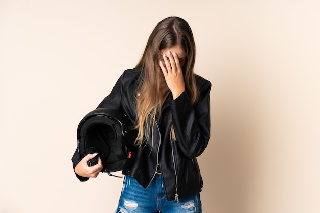 Giovane donna lituana che tiene un casco da motociclista isolato su beige con espressione stanca e malata