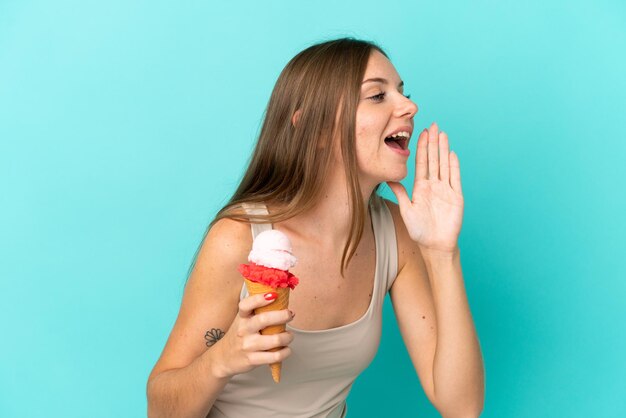 Giovane donna lituana con gelato alla cornetta isolato su sfondo blu che grida con la bocca spalancata di lato