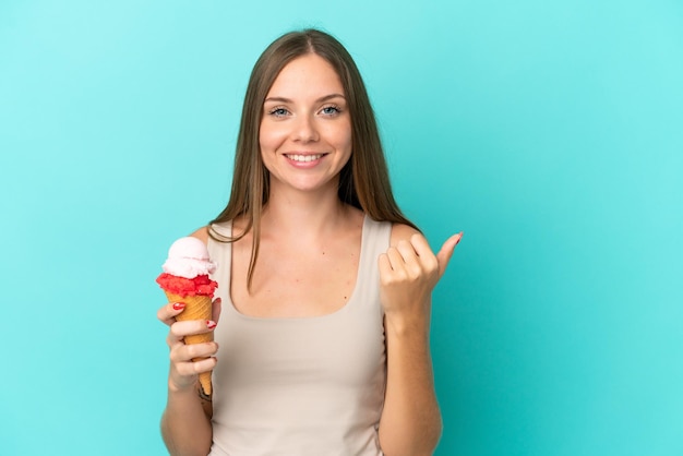 Giovane donna lituana con gelato alla cornetta isolato su sfondo blu che indica il lato per presentare un prodotto