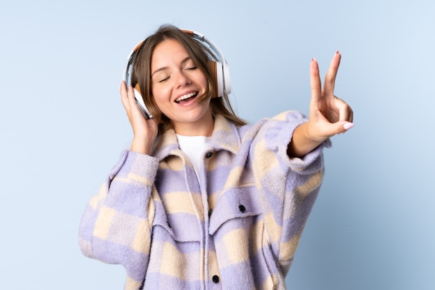 Giovane donna lituana isolata su sfondo blu ascoltando musica e cantando