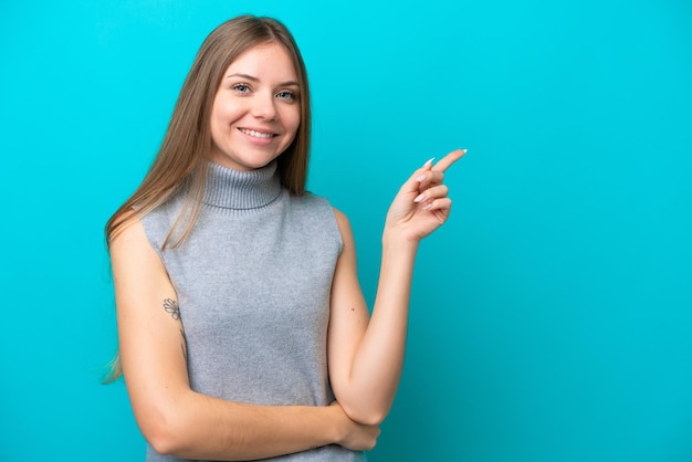 Giovane donna lituana isolata su sfondo blu che punta il dito di lato
