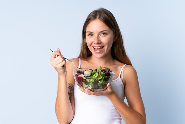 Giovane donna lituana isolata su sfondo blu, tenendo una ciotola di insalata con felice espressione