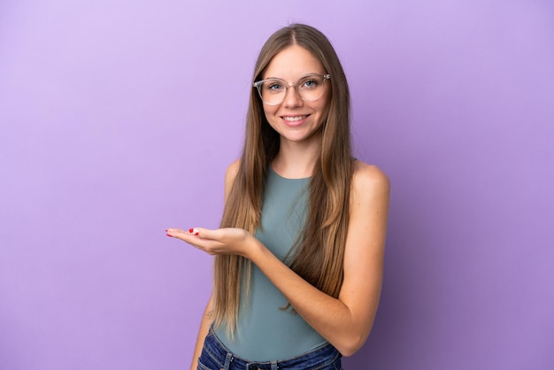 Giovane donna lituana isolata su sfondo viola che presenta un'idea mentre guarda sorridendo verso