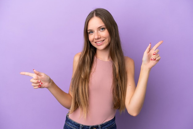 Giovane donna lituana isolata su sfondo viola che punta il dito verso i laterali e felice