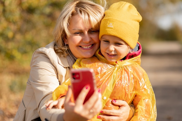 Giovane donna, madre di una bambina, usa lo smartphone per fare videochiamate ai suoi parenti o si fa un selfie nel mezzo del parco autunnale