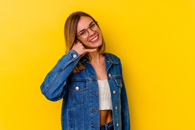 Giovane donna magra caucasica isolata su giallo che mostra un gesto di chiamata di telefono cellulare con le dita.