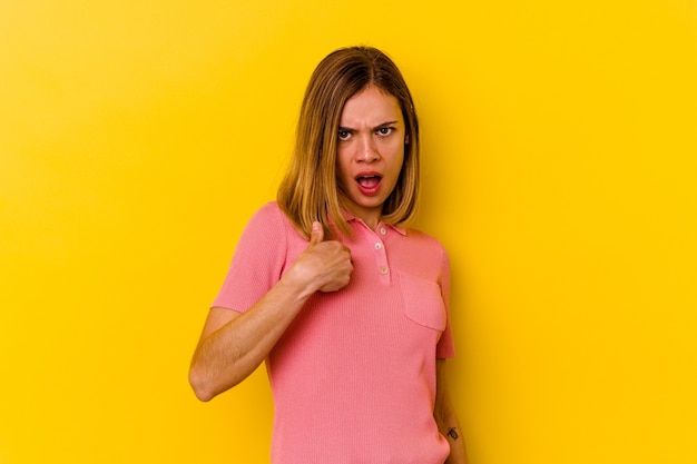 Giovane donna magra caucasica isolata sul muro giallo sorpreso indicando con il dito, sorridendo ampiamente.