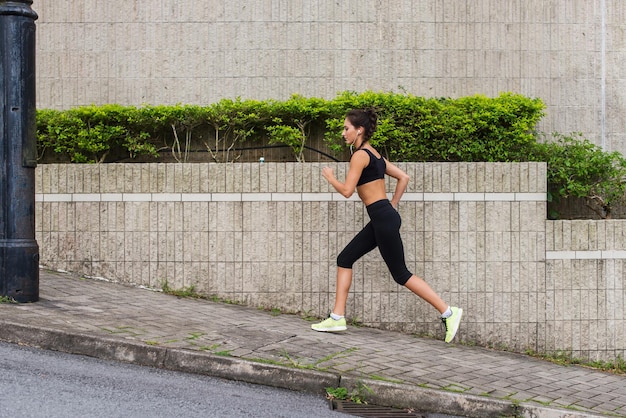 Giovane donna magra che corre in salita sul marciapiede della strada della città Atleta femminile che si allena all'esterno