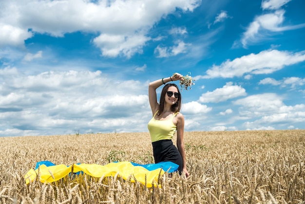 Giovane donna magra in bandiera blu-gialla dell'Ucraina sul campo di grano in estate