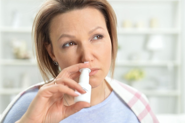 Giovane donna malata con naso tappato usando spray nasale