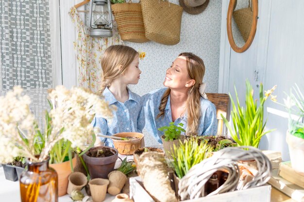 giovane donna mamma e la sua bambina in famiglia look abiti stanno piantando fiori sulla terrazza primaverile in casa giardino piantine in crescita casa di campagna veranda maternità