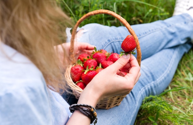 Giovane donna mangia fragole mature seduta sull'erba concetto di stile di vita sano attenzione selettiva
