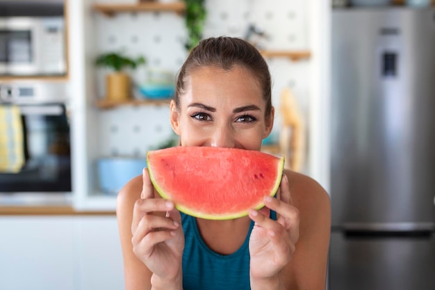 Giovane donna mangia una fetta di cocomero in cucina Ritratto di giovane donna che si gode un cocomero