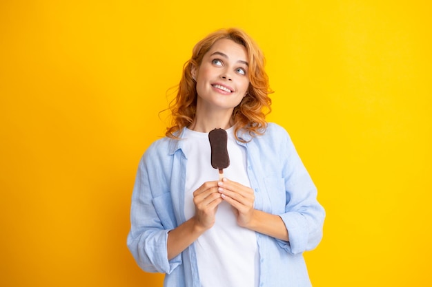 Giovane donna mangiare gelati con glassa di cioccolato su sfondo giallo Divertente donna rossa gelato