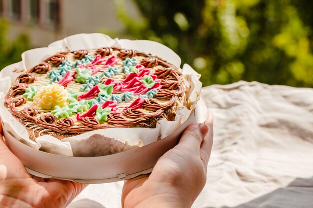 Giovane donna mani appena aperto tradizionale Kiev intera torta di noci nella confezione. I noti prodotti da forno ucraini. Giornata di sole e sfondo verde.