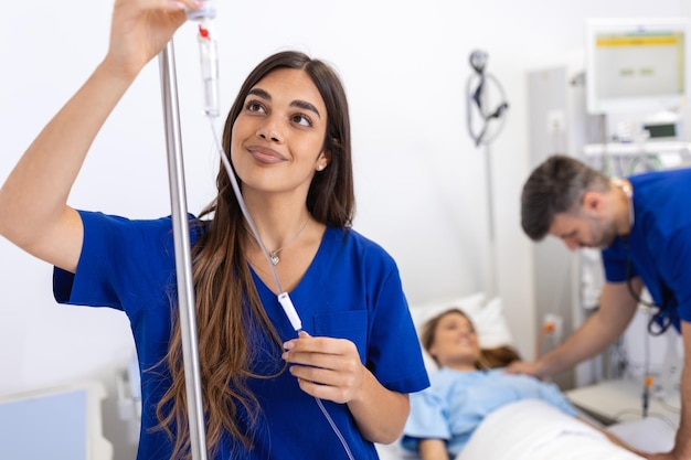 Giovane donna medico anestesista vestita di abito blu mette il contagocce IV nella stanza d'ospedale