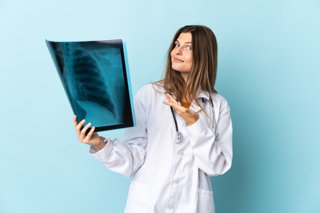 Giovane donna medico che tiene la radiografia sopra la parete isolata che estende le mani al lato per invitare a venire