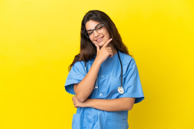Giovane donna medico chirurgo isolata su sfondo giallo sorridente
