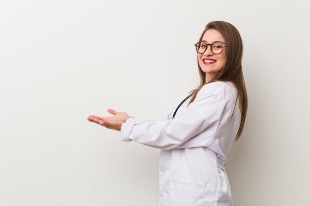 Giovane donna medico contro un muro bianco in possesso di uno spazio di copia su una palma.