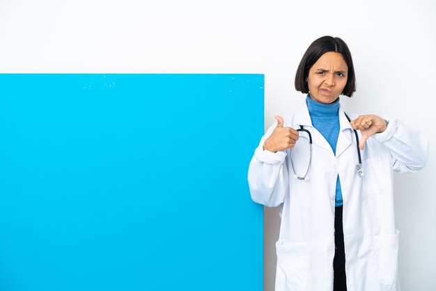 Giovane donna medico di razza mista con un grande cartello isolato su sfondo bianco che fa segno buono-cattivo. Indeciso tra sì o no