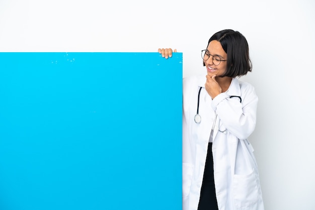 Giovane donna medico di razza mista con un grande cartello isolato su sfondo bianco guardando di lato e sorridente