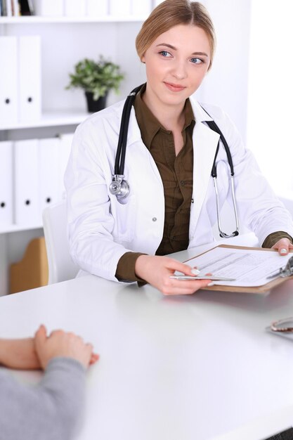 Giovane donna medico e paziente alla visita medica nell'ufficio dell'ospedale. La camicetta color kaki del terapeuta sta bene. Medicina, assistenza sanitaria e concetto di appuntamento del medico.