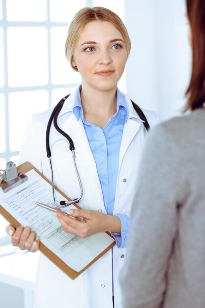 Giovane donna medico e paziente alla visita medica presso l'ufficio dell'ospedale. La camicetta blu del terapeuta sembra buona. Concetto di medicina e assistenza sanitaria.