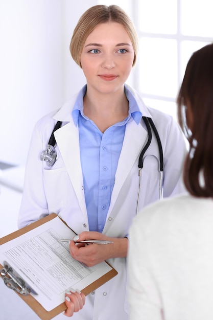 Giovane donna medico e paziente alla visita medica presso l'ufficio dell'ospedale. La camicetta blu del terapeuta sembra buona. Concetto di medicina e assistenza sanitaria.