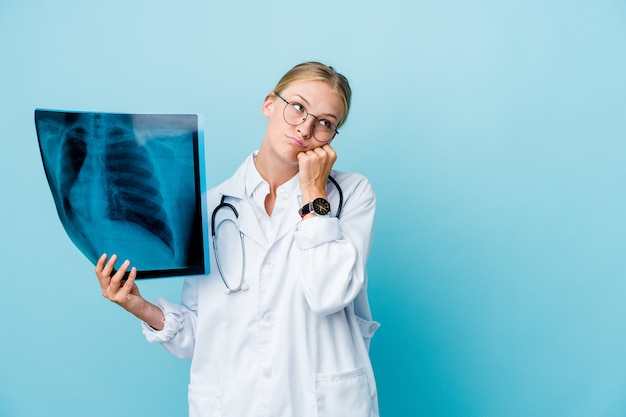 Giovane donna medico russo che tiene una scintigrafia ossea sul blu che si sente triste e pensieroso, guardando lo spazio della copia.