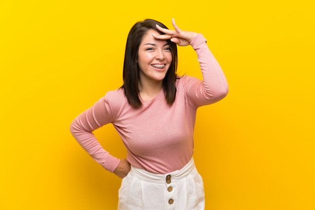 Giovane donna messicana su sfondo giallo isolato guardando lontano con la mano per guardare qualcosa