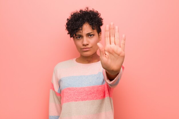 Giovane donna mista afroamericana dell'adolescente che sta con il fanale di arresto di rappresentazione della mano tesa, impedendovi.