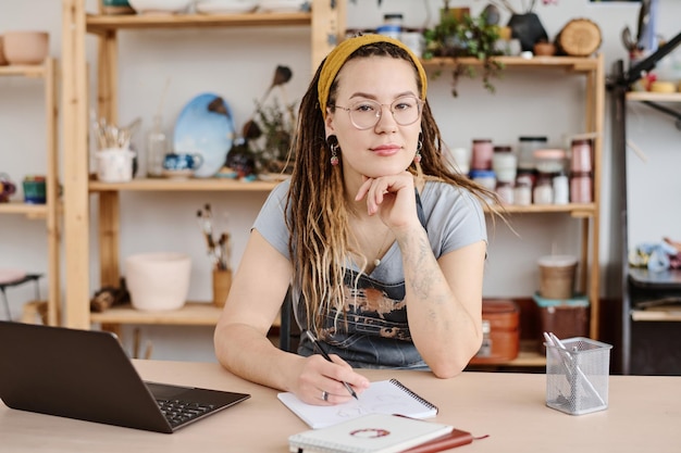 Giovane donna moderna in abbigliamento casual e occhiali seduti sul posto di lavoro
