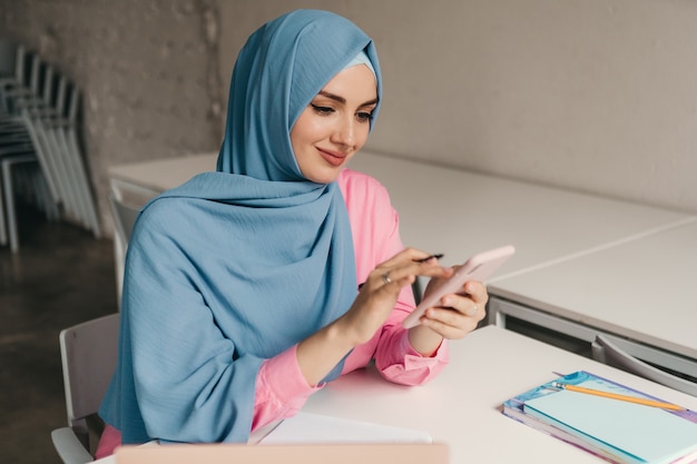 Giovane donna musulmana abbastanza moderna in hijab che lavora al computer portatile nella stanza dell'ufficio, istruzione online