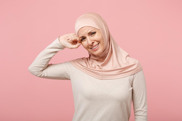 Giovane donna musulmana araba dispiaciuta in abiti leggeri hijab in posa isolata su sfondo rosa, ritratto in studio. Concetto di stile di vita dell'Islam religioso della gente. Mock up spazio di copia. Piangere, asciugarsi le lacrime.