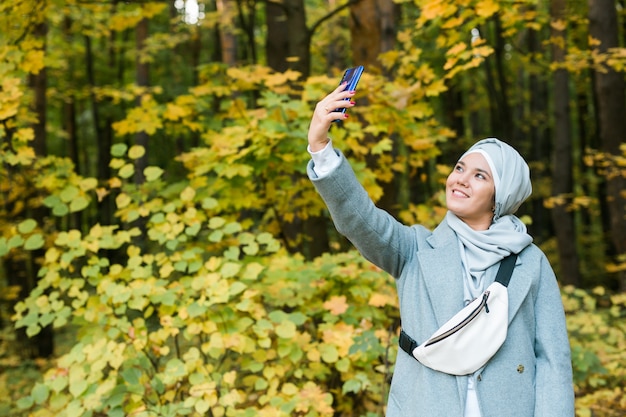 Giovane donna musulmana araba in abiti hijab che fa selfie sparato sul telefono cellulare nel parco persone