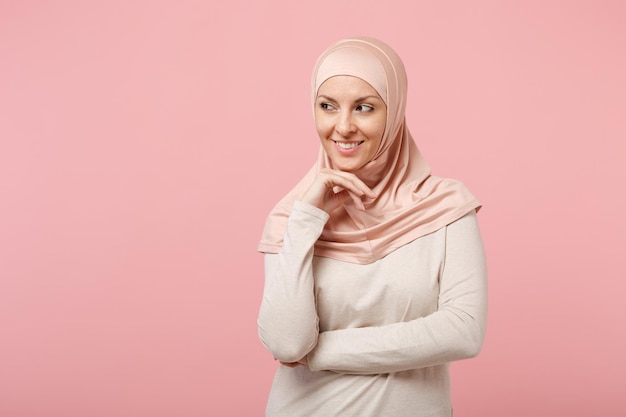 Giovane donna musulmana araba pensierosa in abiti leggeri hijab in posa isolata su sfondo rosa. Concetto di stile di vita dell'Islam religioso della gente. Mock up spazio di copia. Guardando da parte e metti la mano sul mento.