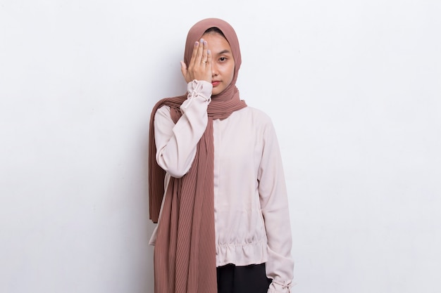 Giovane donna musulmana asiatica che copre un occhio con la mano isolata su sfondo bianco