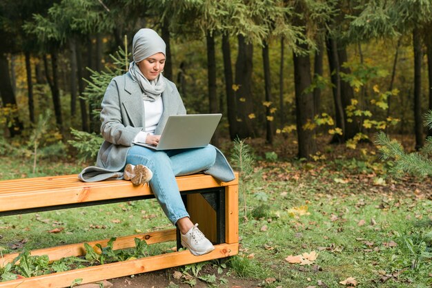 Giovane donna musulmana asiatica che utilizza il computer portatile all'istruzione online del parco autunnale, shopping online e social