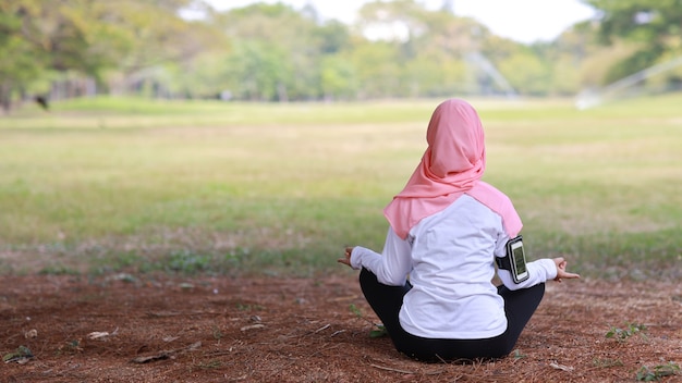 Giovane donna musulmana asiatica di retrovisione che si siede sull'erba, godendo della meditazione