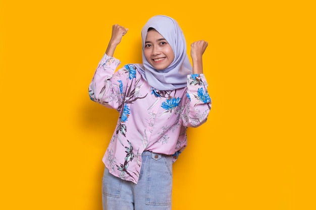 giovane donna musulmana asiatica felice di celebrare la vittoria esprimendo un grande successo su sfondo giallo