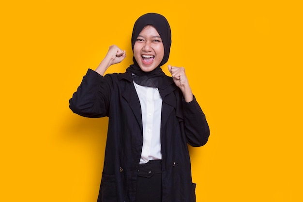 giovane donna musulmana asiatica felice ed eccitata che celebra la vittoria esprimendo un grande successo sul giallo