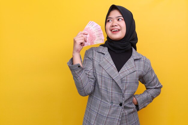 Giovane donna musulmana asiatica in hijab che tiene banconote in valuta indonesiana Rupiah con felice ex