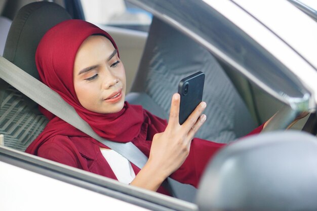 Giovane donna musulmana asiatica in hijab che usa lo smartphone sorridente in macchina