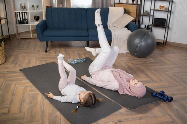 Giovane donna musulmana che fa esercizi di flessibilità di stretching insieme a sua figlia in età prescolare